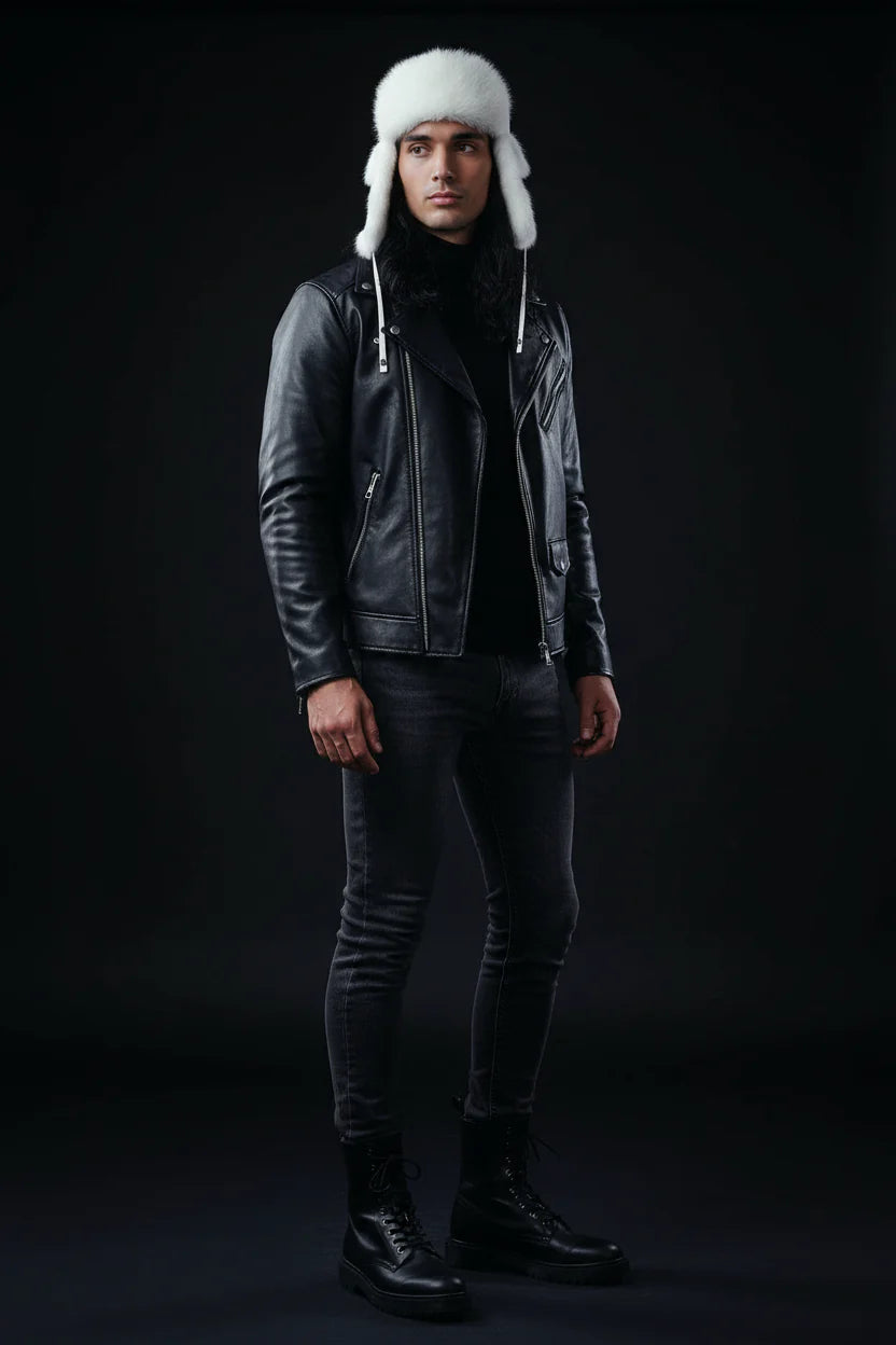Person wearing a black leather jacket, dark pants, and a white fur hat on a black background