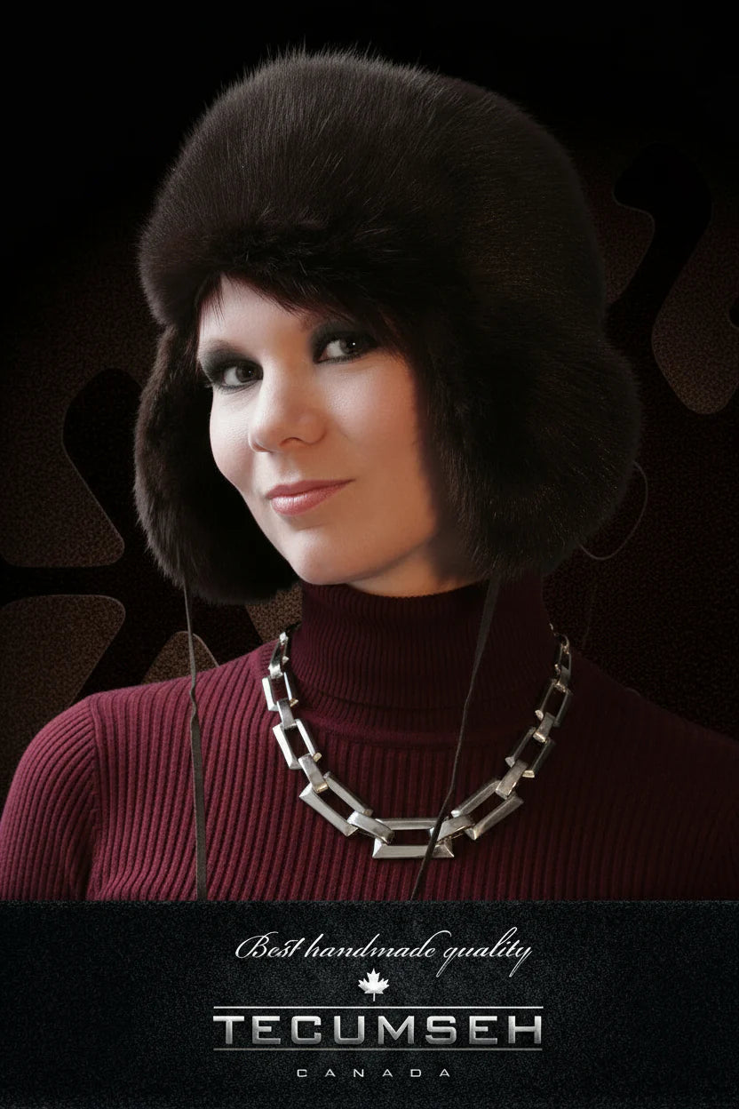 Woman wearing a dark muskrat fur hat and maroon sweater with a necklace, against a dark background with 'Tecumseh Canada' branding.