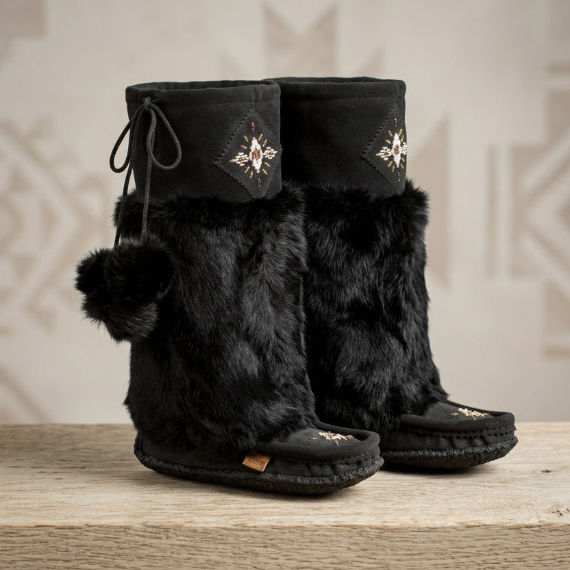 Black furry boots with decorative elements on a wooden surface and neutral background