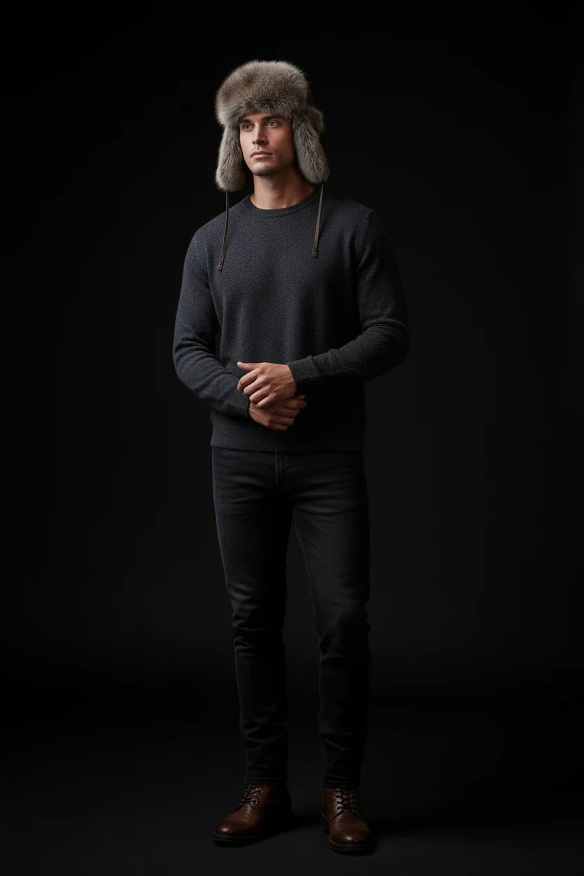 Man wearing a dark sweater, gray fur hat, and dark pants against a black background
