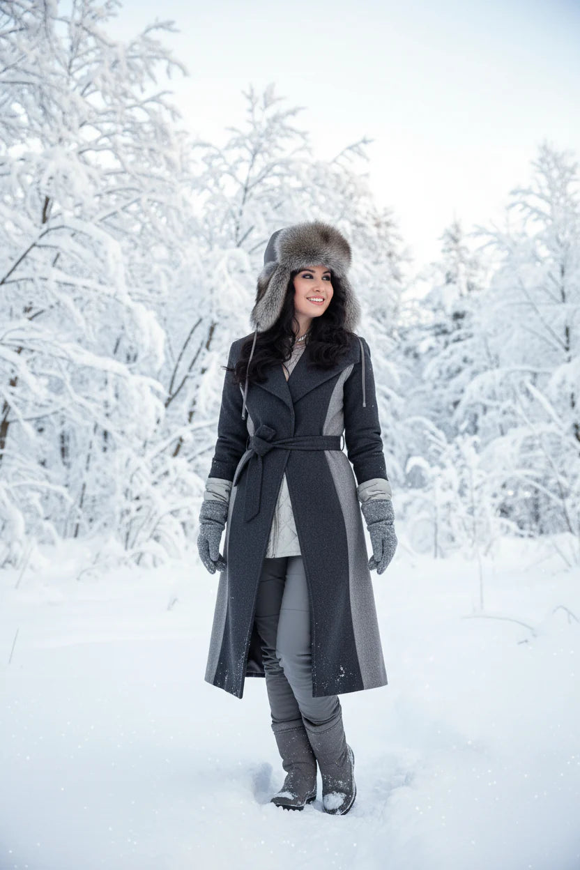 Woman in a long dark coat and fur hat standing in a snowy forest
