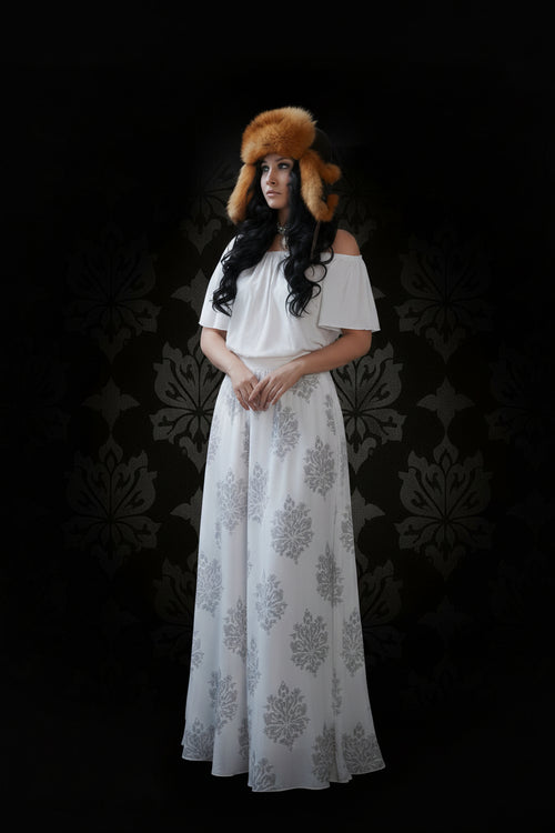 Woman wearing a white off-shoulder top and long floral skirt with a fur hat against a dark background
