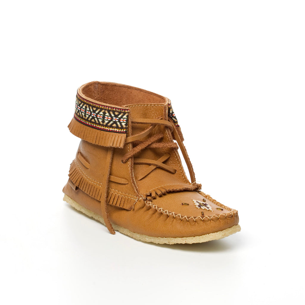 Brown moccasin shoe with decorative elements on a wooden surface with pebbles in the background